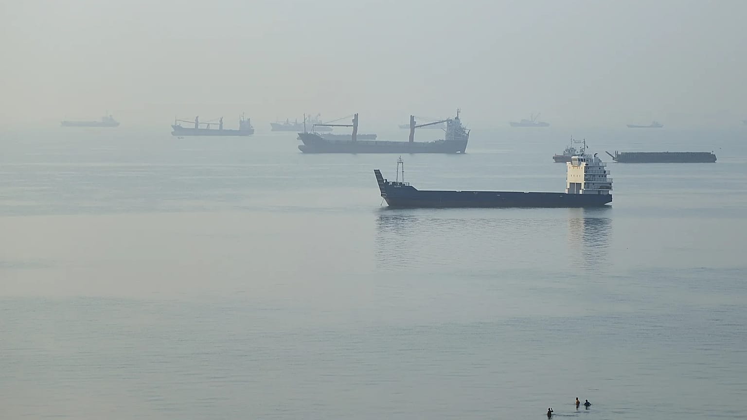 People wade in the water as cargo ships are anchored in the Strait of Hormuz off Bandar Abbas, Iran, early Monday, Sept. 28, 2026.