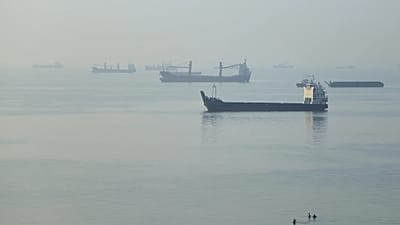 Des personnes marchent dans l'eau tandis que des cargos sont à l'ancre dans le détroit d'Ormuz, au large de Bandar Abbas, en Iran, tôt le lundi 28 septembre 2026.