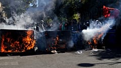 Protesters stand behind burning garbage cans during an anti-government demonstration outside the Education Ministry, in Tirana, Albania, Saturday, Oct. 17, 2026.