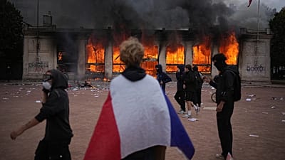 A protester wraps a French flag around them in front of the burning tourism office during a demonstration in Lyon, France, Saturday, Oct. 17, 2026.