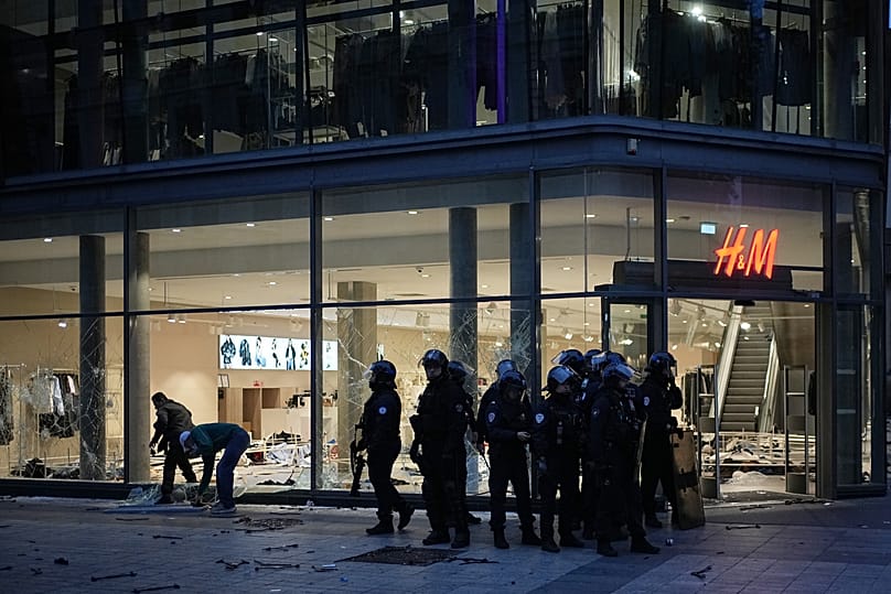 Police officers stand guard in front of a looted store during a demonstration against rising living costs, joining students' grievances, in Lyon, France, Saturday, Oct. 17.