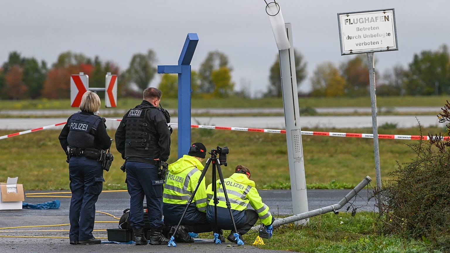 Police officers inspect the site of a damaged fence section at the entrance to the Leipzig/Halle airport grounds, 18 October, 2026