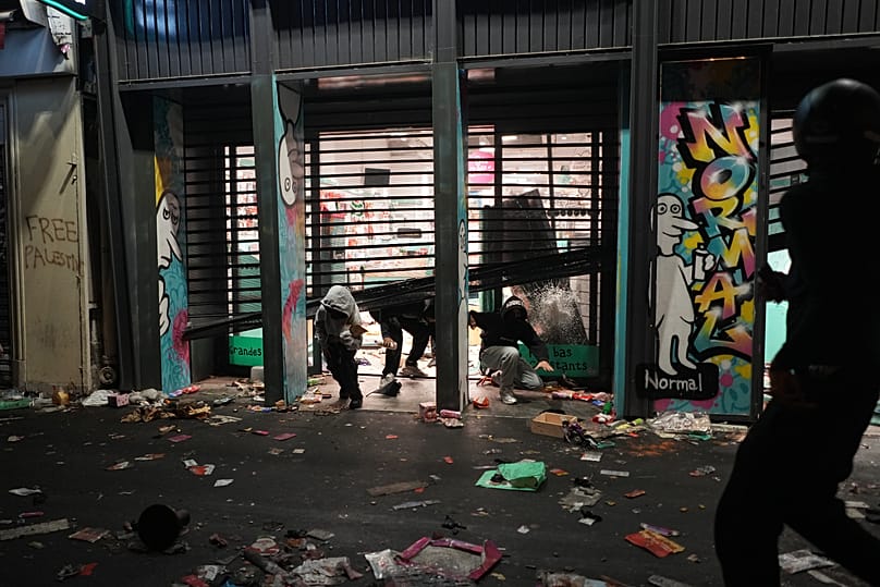 Demonstrierende kommen aus einem geplünderten Laden während eines Protests gegen steigende Lebenshaltungskosten und schließen sich den Forderungen von Studierenden an, in Paris, Samstag, 17. Oktober 2026.