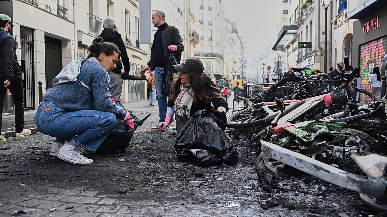 Περαστικοί απομακρύνουν συντρίμμια σε δρόμο δίπλα σε καμένα ποδήλατα, την επομένη διαδήλωσης κατά της ακρίβειας και υπέρ φοιτητών, στο Παρίσι.