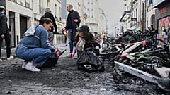 People clean up debris in a street next to burned bicycles the day after a demonstration against rising living costs and in solidarity with students' grievances, in Paris