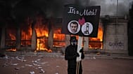 Un manifestant tient une pancarte avec une photo d'Emmanuel Macron devant un office de tourisme en feu lors d'une manifestation contre la vie chère à Lyon.