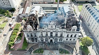 Демонстрант держит плакат с фотографией Эмманюэля Макрона перед горящим туристическим офисом во время акции против роста цен в Лионе, Франция, в субботу, 17 октября 2026 года.
