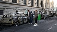 FILE. People look at a charred car near Place de la Republique the day after protests against rising living costs in Paris, 18 Oct. 2026