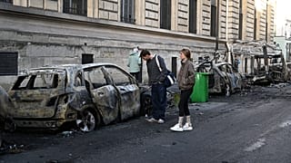 FILE. People look at a charred car near Place de la Republique the day after protests against rising living costs in Paris, 18 Oct. 2026