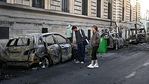 FILE. People look at a charred car near Place de la Republique the day after protests against rising living costs in Paris, 18 Oct. 2026