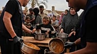 فلسطينيون يتسلمون مواد غذائية تبرع بها برنامج الأغذية العالمي في مخيم للنازحين في دير البلح، وسط قطاع غزة