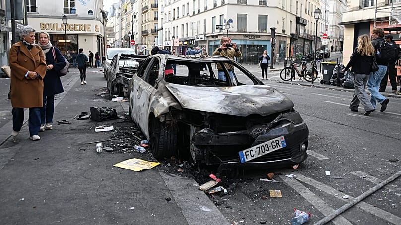 Des passants observent des voitures calcinées au lendemain d'une manifestation à Paris, le 18 octobre 2026