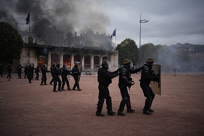La police anti-émeute fait face aux manifestants devant l'office du tourisme incendié, sur la place Bellecour, à Lyon, le samedi 17 octobre 2026. 