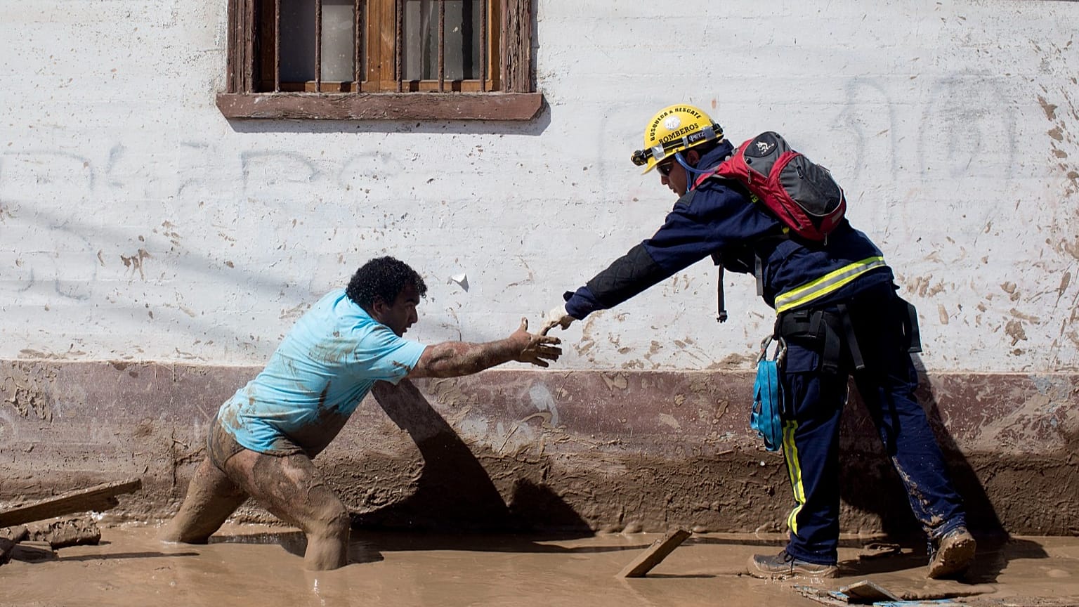 ARCHIVO: Un rescatista extiende su mano para ayudar a un lugareño a cruzar una calle cubierta de lodo en Chanaral, Chile, en marzo de 2015.