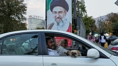 رجل وامرأة يستقلان سيارة، ويمرّان أمام صورة للمرشد الأعلى الإيراني مجتبى خامنئي في العاصمة طهران، الأربعاء 21 تشرين الأول/أكتوبر 2026. 