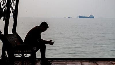 Un hombre mira su móvil en un refugio costero mientras buques mercantes están anclados en el estrecho de Ormuz, frente a Bandar Abbas, Irán, 6 oct. 2026. (Amirho