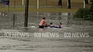 People climb onto a submerged car that is sinking to rescue the driver.