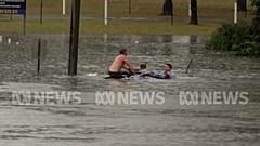 People climb onto a submerged car that is sinking to rescue the driver.