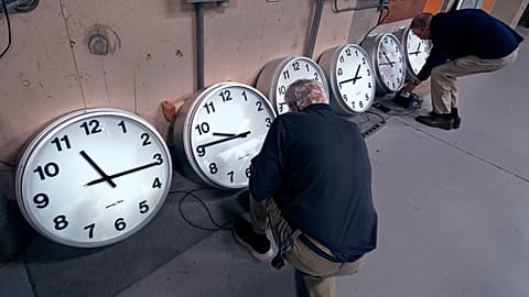 FILE: Clockmakers Rich Finn, left, and Tom Erb adjust the time zone controllers on a series of clocks.