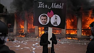 Manifestante com cartaz anti-Macron, com a sede do turismo de Lyon em chamas