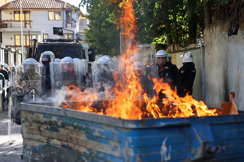 Riot police stand in formation behind a burning garbage can during an anti-government rally, in Tirana, Albania, Saturday, Oct. 24, 2026. (AP Photo/Hameraldi Agolli)