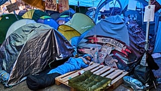 ARCHIVO: Un hombre duerme en un campamento improvisado en la Puerta del Sol en Madrid, España, el sábado 17 de octubre de 2026.