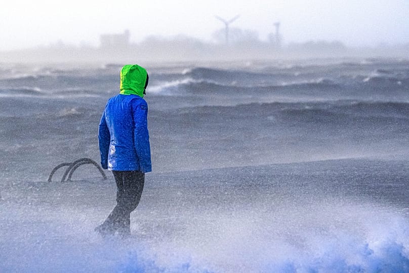 Eine Person geht am Freitag, dem 22. Dezember 2023, in Bremerhaven am Ufer der Wesermündung entlang, während dort eine Sturmflut herrscht.