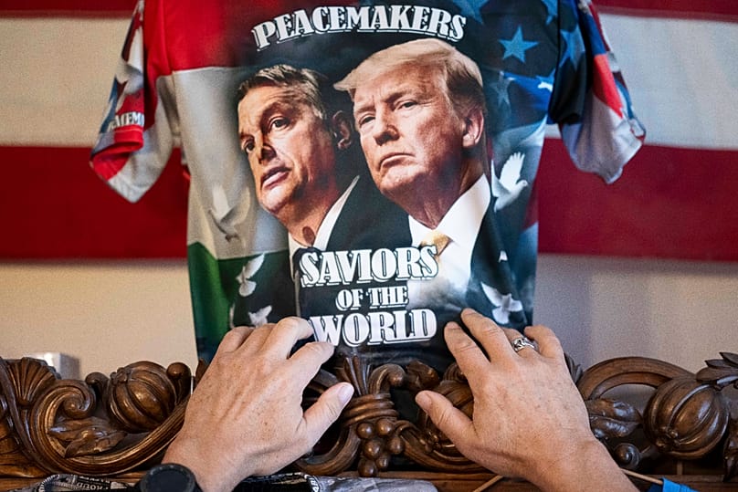 Szilágyi Ákos, Orbán Viktor egyik legnagyobb rajongója 2026. április 14-én budapesti otthonában igazítja meg az általa tervezett pólóját, amelyen Orbán és Donald