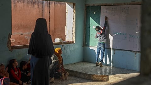 A pupil writes on the whiteboard as classmates and their teacher watch during a lesson at "Maar Shamarin" Primary School, whose walls still bear bullet holes from the war.