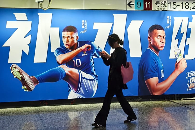 A woman walks by an advertisement featuring French soccer star Kylian Mbappé in Shanghai, China on June 30, 2026. (Chinatopix Via AP) CHINA OUT