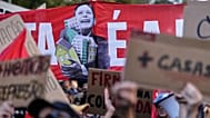 Um cartaz com a imagem de Luís Montenegro a abraçar um conjunto de casas durante um protesto para exigir habitação acessível em Lisboa no sábado, 24 de outubro de 2026
