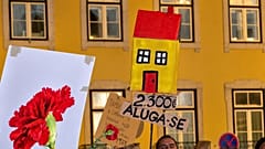 Manifestantes erguem uma casa de cartão e um cartaz onde se lê: “ARRENDA-SE: 2 300 €”