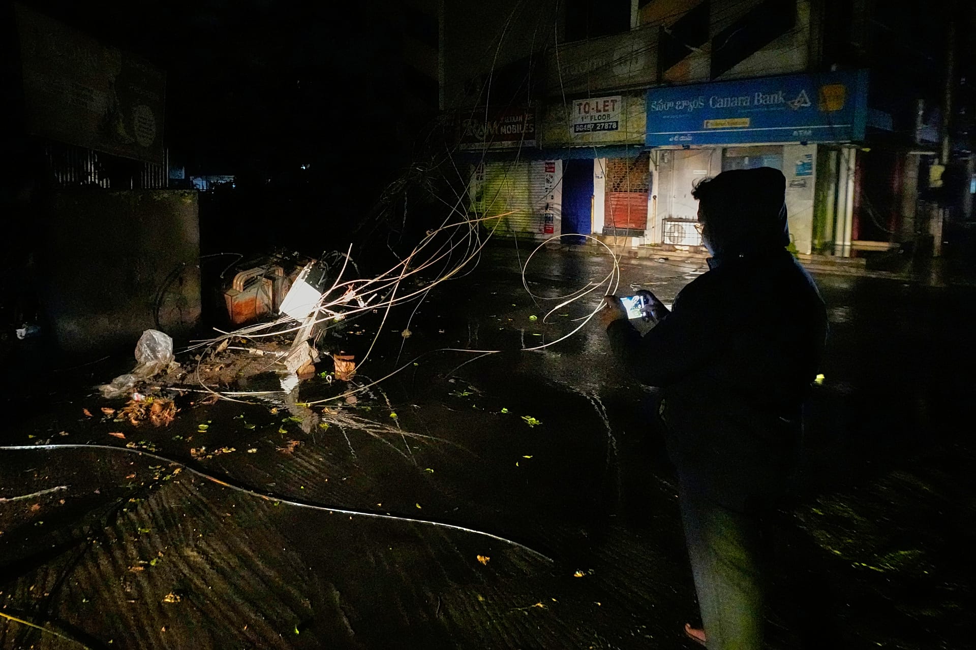 A man films an electrical transformer toppled by heavy rain and strong winds as Cyclone Arnab approaches the Andhra Pradesh coast in Kakinada, India, Tuesday, O