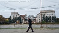 A man walks beneath anti-drone nets stretched over a street in front of a destroyed regional administration building during a ceasefire in Kherson, Ukraine, Oct. 27, 2026. 