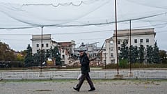 Homem passa sob redes antidrone estendidas sobre uma rua junto a edifício destruído da administração regional, durante cessar-fogo em Kherson, Ucrânia, 27 de outubro de 2026