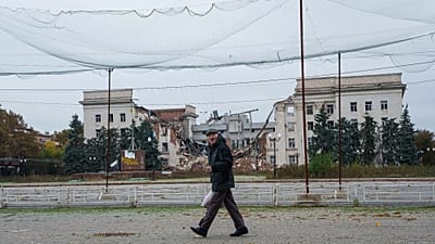 A man walks beneath anti-drone nets stretched over a street in front of a destroyed regional administration building during a ceasefire in Kherson, Ukraine, Oct. 27, 2026. 