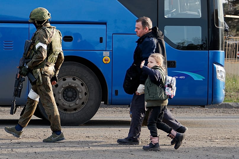 Azovstal'daki bir sığınaktan çıkan bir adam ile bir kız çocuğu, 6 Mayıs 2022'de Ukrayna'nın Mariupol kentinde Rus Ordusu mensubu bir asker eşliğinde otobüse doğru yürüyor.