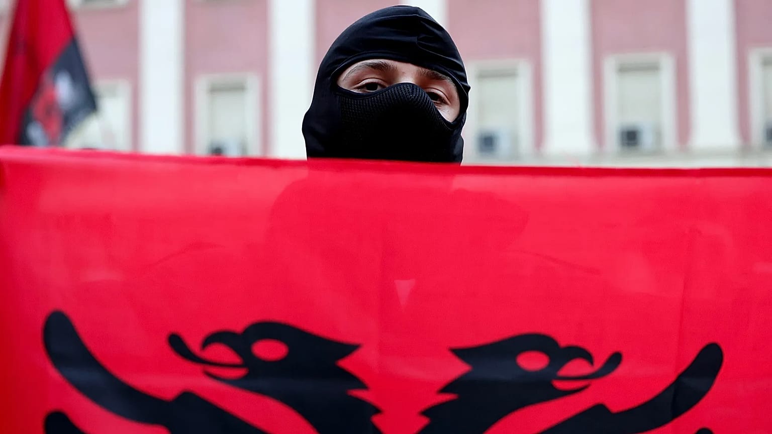 A masked protester holds an Albanian flag during an anti-government rally in Tirana, Albania, Sunday, 25 Oct., 2026