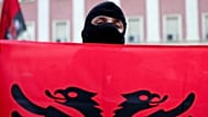 A masked protester holds an Albanian flag during an anti-government rally in Tirana, Albania, Sunday, 25 Oct., 2026