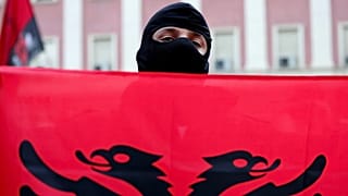 A masked protester holds an Albanian flag during an anti-government rally in Tirana, Albania, Sunday, 25 Oct., 2026