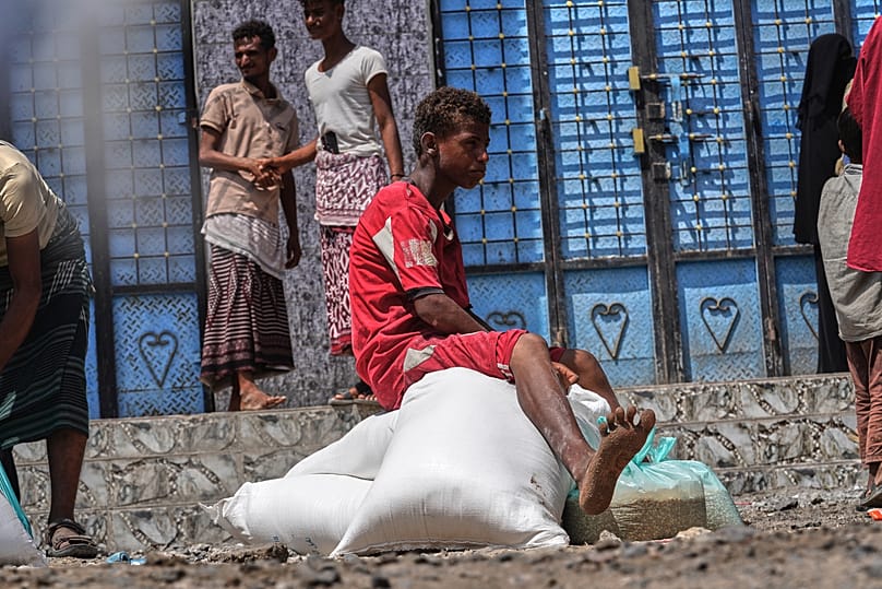 صبي يمني نازح يجلس فوق أكياس من المساعدات الغذائية في منطقة صلاح الدين بضواحي عدن