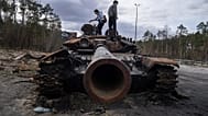 Local residents stand atop of a Russian tank damaged during fightings between Russian and Ukrainian forces in the outskirts of Kyiv, Ukraine, Monday, April 11, 2022.