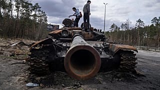Local residents stand atop of a Russian tank damaged during fightings between Russian and Ukrainian forces in the outskirts of Kyiv, Ukraine, Monday, April 11, 2022.