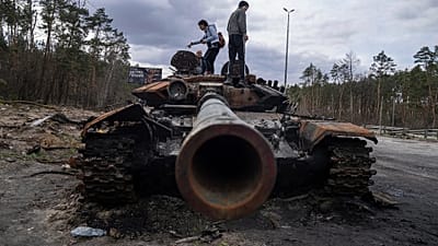 Local residents stand atop of a Russian tank damaged during fightings between Russian and Ukrainian forces in the outskirts of Kyiv, Ukraine, Monday, April 11, 2022.