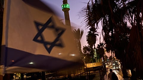 The minaret of the Hassan Bek Mosque stands in the background as a pedestrian passes an Israeli flag in Tel Aviv, Israel, Thursday, Oct. 29, 2026.