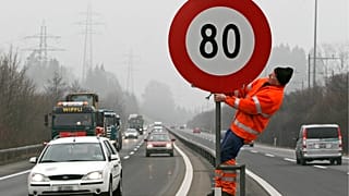 Archivfoto. Ein Arbeiter stellt am Freitag, dem 3. Februar 2006, auf der Autobahn N4 in Zug (Schweiz) ein Schild auf, das eine Geschwindigkeitsbegrenzung von 80 km/h anzeigt.