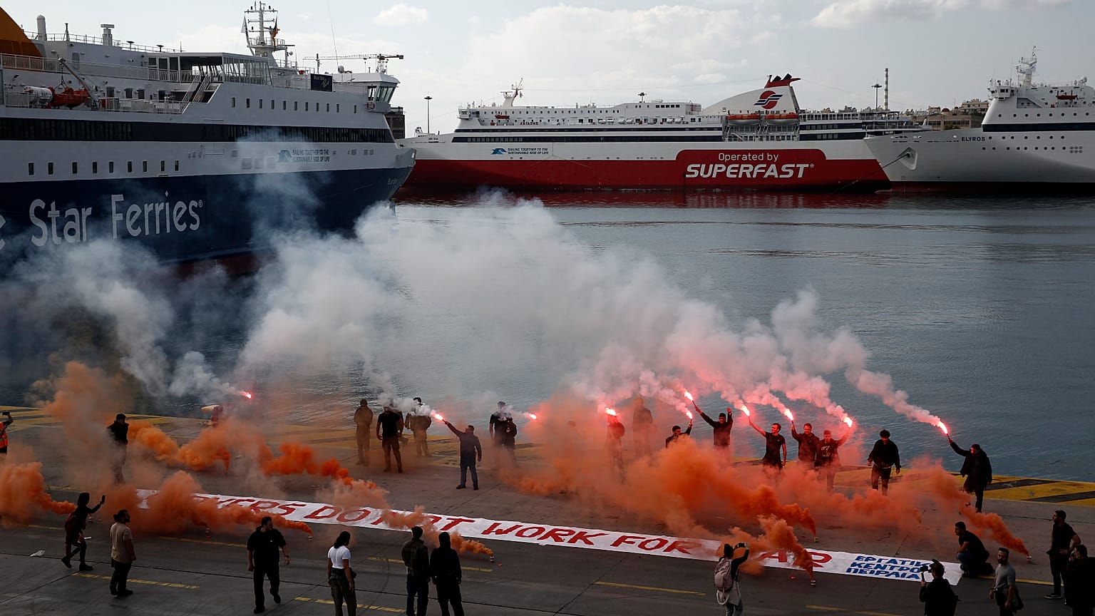 Μέλη ναυτεργατικών σωματείων κρατούν καπνογόνα κατά τη διάρκεια συγκέντρωσης διαμαρτυρίας στο λιμάνι του Πειραιά, με κεντρικό σύνθημα «Οι λιμενεργάτες δεν δουλεύουμε για τον π