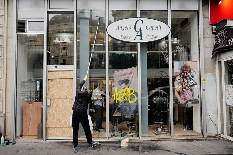 Ein Mann reinigt den beschädigten Schaufensterbereich eines Friseursalons nach Ausschreitungen und Plünderungen in Paris, Mittwoch, 21. Oktober 2026.